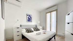 Une chambre à coucher comprenant un lit, des tables de chevet, un climatiseur fixé au mur et une fenêtre avec des rideaux.