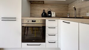 Une cuisine moderne avec des meubles blancs, un four encastré et un pare-feu en bois.