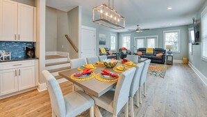 Una cocina moderna con armarios blancos, un salpicadero azul y un comedor con una mesa de madera dispuesta para cuatro.