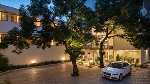 A modern building with a paved driveway, a white car parked in front, and a tree in the center. - Time Square Boutique Hotel (Ambalapuzha)