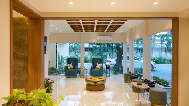 A modern lobby with a marble floor, two green armchairs, a round coffee table, and a view of the outside through large windows. - Time Square Boutique Hotel (Ambalapuzha)