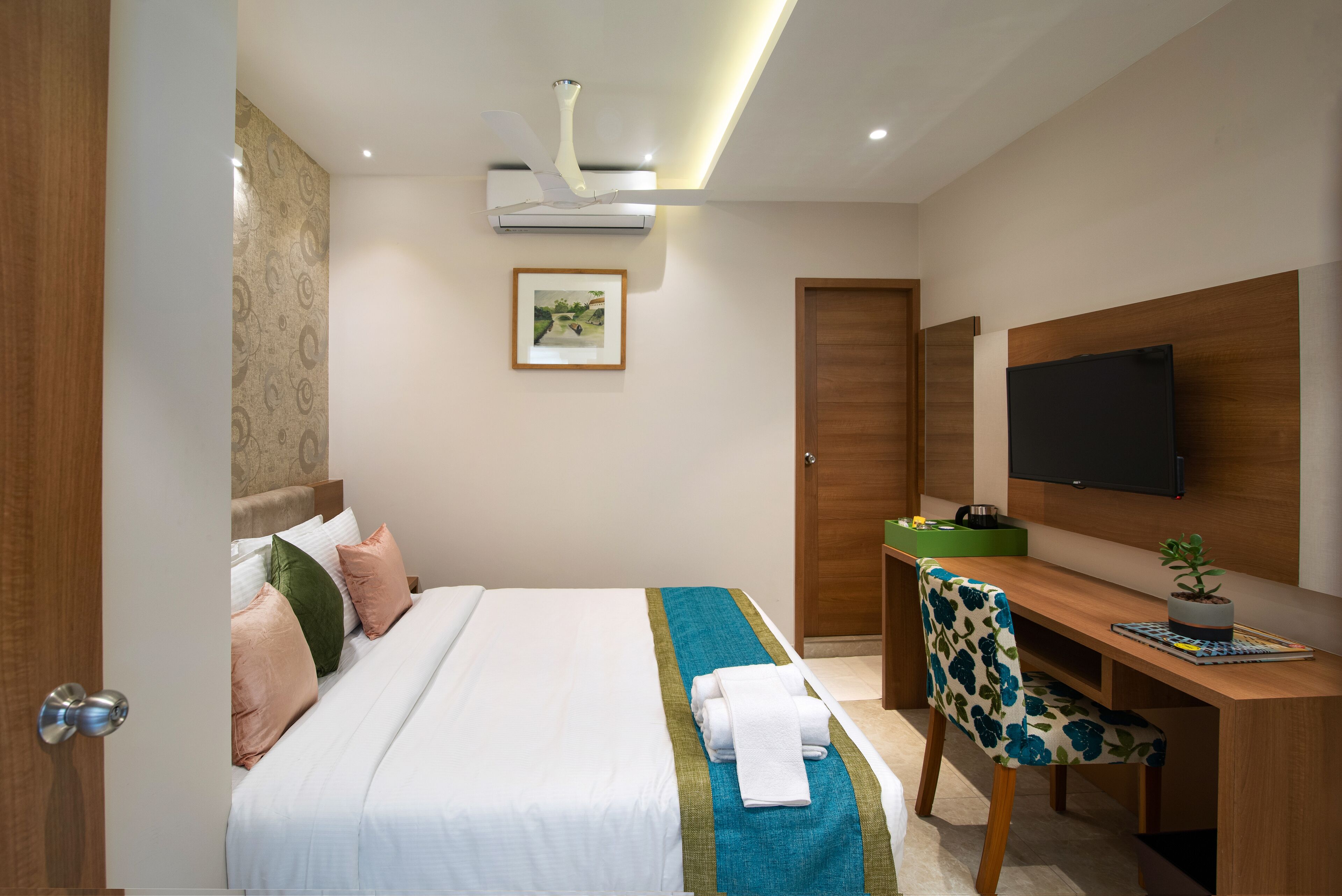 A hotel room with a bed, a desk, a chair, a television, and a door.