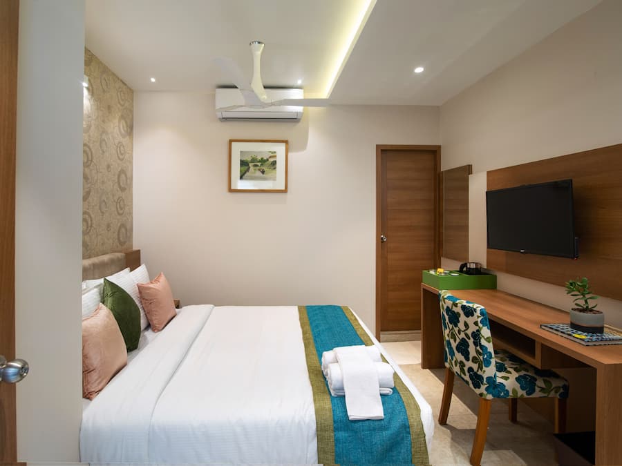 Una habitación de hotel con cama, escritorio, silla, televisor y puerta.