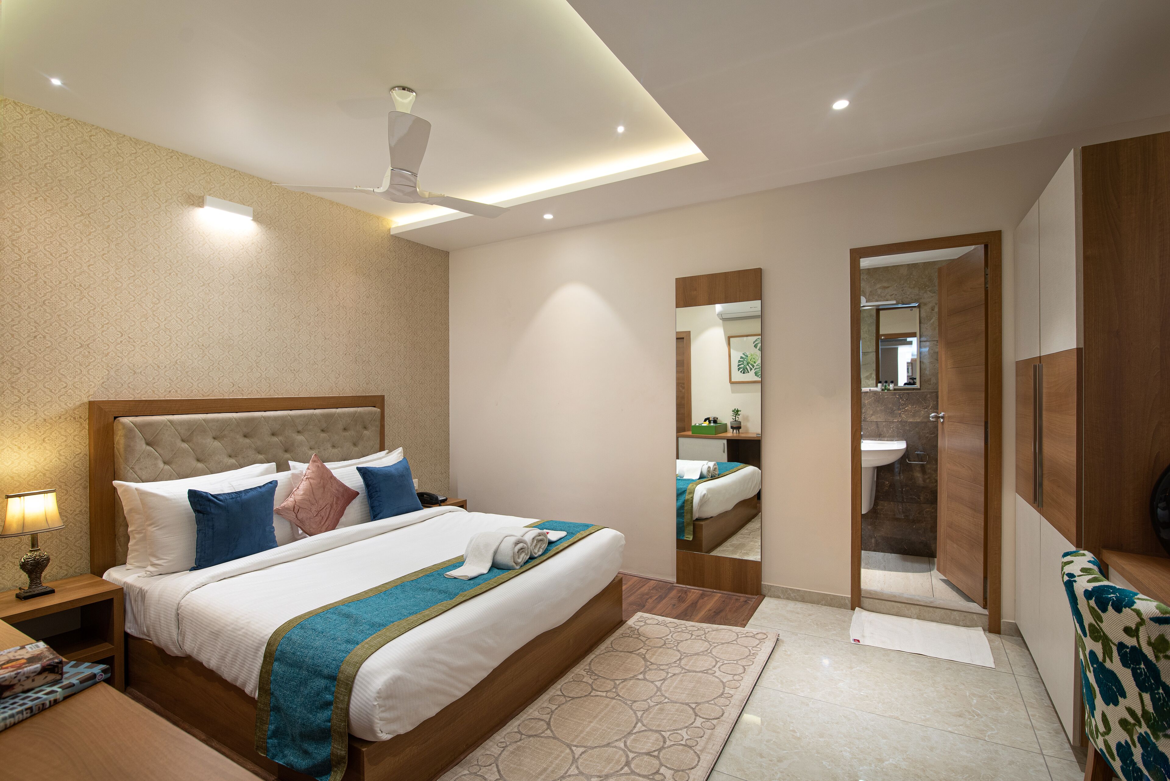 A modern hotel room with a large bed, bedside table, and a mirror.