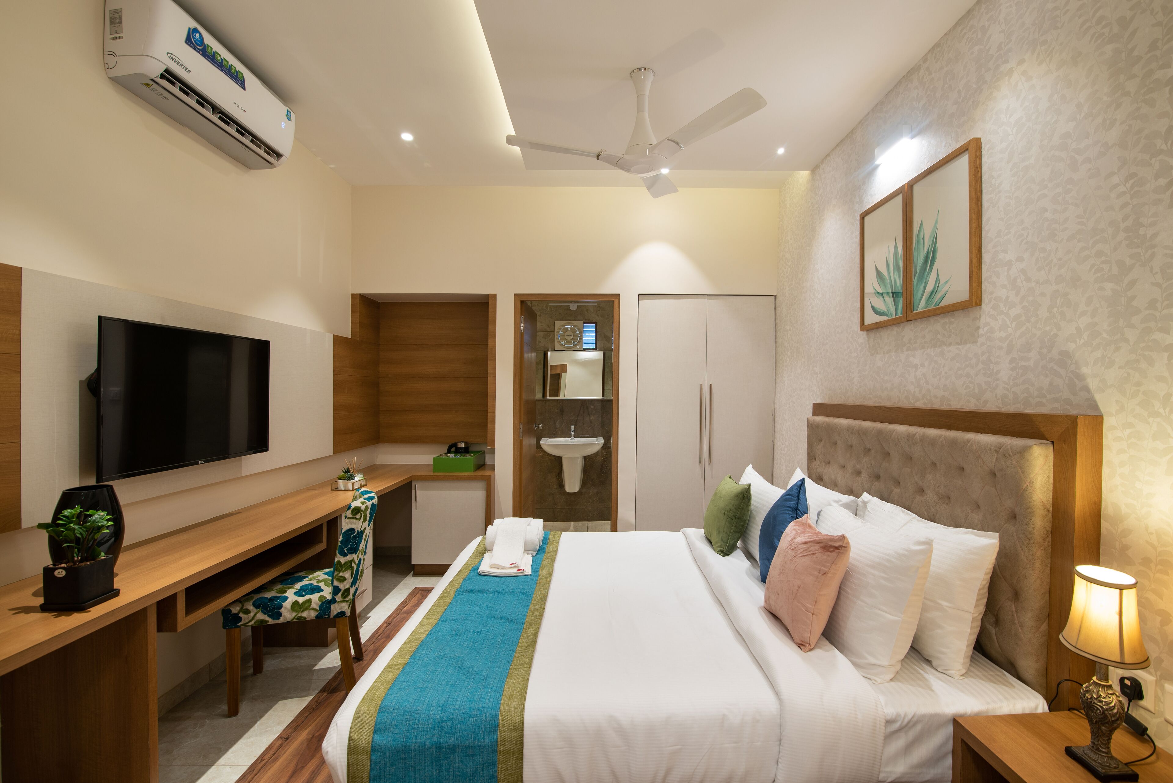 Una habitación de hotel con cama, escritorio, televisor y ventilador de techo.