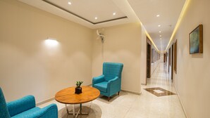 A hallway with a blue armchair, a round wooden table with a plant, and a ceiling with recessed lighting. - Time Square Boutique Hotel (Ambalapuzha)