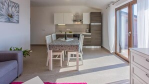 A modern kitchen with white cabinets, a dining table with chairs, and a large window providing natural light. - Modern apartment with terrace and fantastic sea view (Crikvenica)