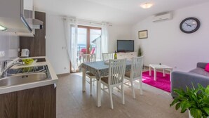 A modern apartment with a kitchen, dining area, and living room. It includes a balcony with a view, a flat-screen TV, and a clock on the wall. - Modern apartment with terrace and fantastic sea view (Crikvenica)