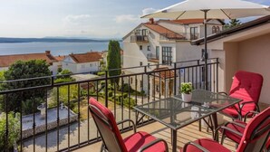 A balcony with red chairs and a table, overlooking a body of water and neighboring buildings. - Modern apartment with terrace and fantastic sea view (Crikvenica)