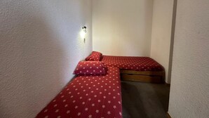 A small, narrow room with two single beds, each with red bedding and white patterns. - 200m from resort center, 4th floor, view ski slopes, swimming pool, balcony, tv, ski locker, 28m² (La Plagne)