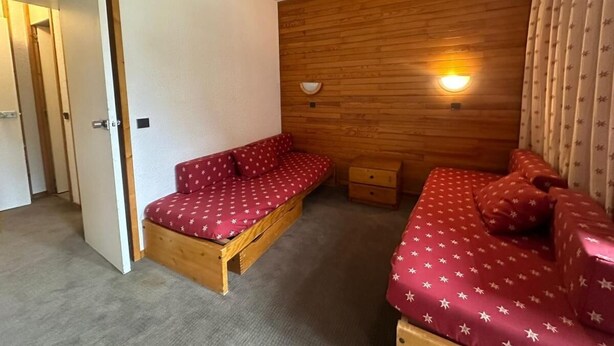A compact room with two beds, a wooden wall panel, a small bedside table, and a wall-mounted light fixture. - 200m from resort center, 4th floor, view ski slopes, swimming pool, balcony, tv, ski locker, 28m² (La Plagne)