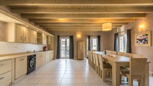 A spacious kitchen with wooden cabinets, a built-in washing machine, and a long dining table with chairs. - Bellavista in Premantura (Medulin)
