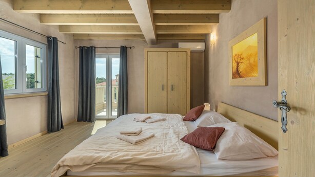 A bedroom with a wooden bed, a wardrobe, a painting on the wall, and a window with curtains. - Bellavista in Premantura (Medulin)