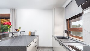 Una cocina moderna con encimera oscura, armarios blancos y ventana con vistas a zonas verdes.