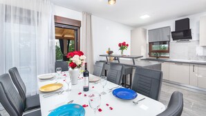 Un comedor moderno con una mesa blanca preparada para cuatro personas, rodeada de sillas negras.
