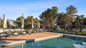 A poolside area with lounge chairs and umbrellas, surrounded by a fence and trees. - Carolus Dalmatia in Vodice (Vodice)