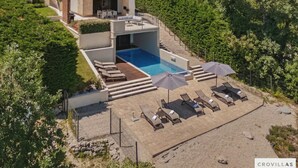 Uma villa moderna com piscina, área de estar externa e vista para uma encosta verde exuberante.