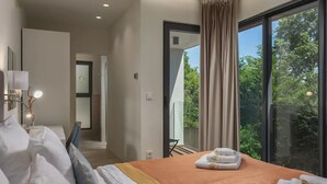 Quarto de hotel moderno com uma cama grande, vista para o verde pela janela e uma varanda.
