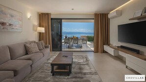 Uma sala de estar moderna com sofá, mesa de centro e televisão. Há uma janela grande com vista para o exterior.