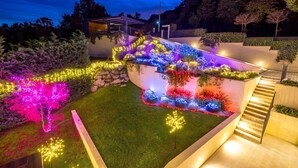 Área externa moderna com escadaria, caminhos iluminados e diversas plantas e árvores.