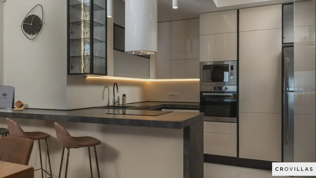 Uma cozinha moderna com uma ilha central, banquetas, forno embutido e micro-ondas.