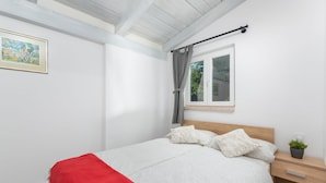 Een slaapkamer met een bed, een nachtkastje, een raam met gordijnen en een schilderij aan de muur.