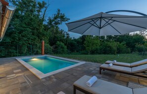 A rectangular swimming pool with a tiled deck, surrounded by lounge chairs and an umbrella. - Matea Labin in Vadre (Barban)