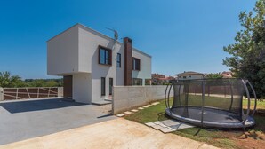 Una casa moderna de dos pisos con techo plano, antena parabólica y un trampolín en el jardín trasero.