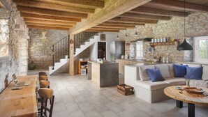 A rustic interior with exposed wooden beams, a stone wall, a kitchen area, and a seating area with a sofa and a round wooden table. - Flavia in Umag With 4 Bedrooms and 3 Bathrooms (Umag)