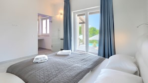A bedroom with a bed, a bathroom, and a view of the outdoors.