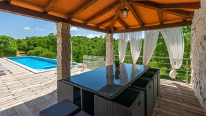 A covered patio with a pool, wicker furniture, and a stone wall.