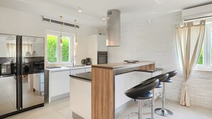 A modern kitchen with a central island, a refrigerator, and a stove. There are three bar stools and a window with curtains.