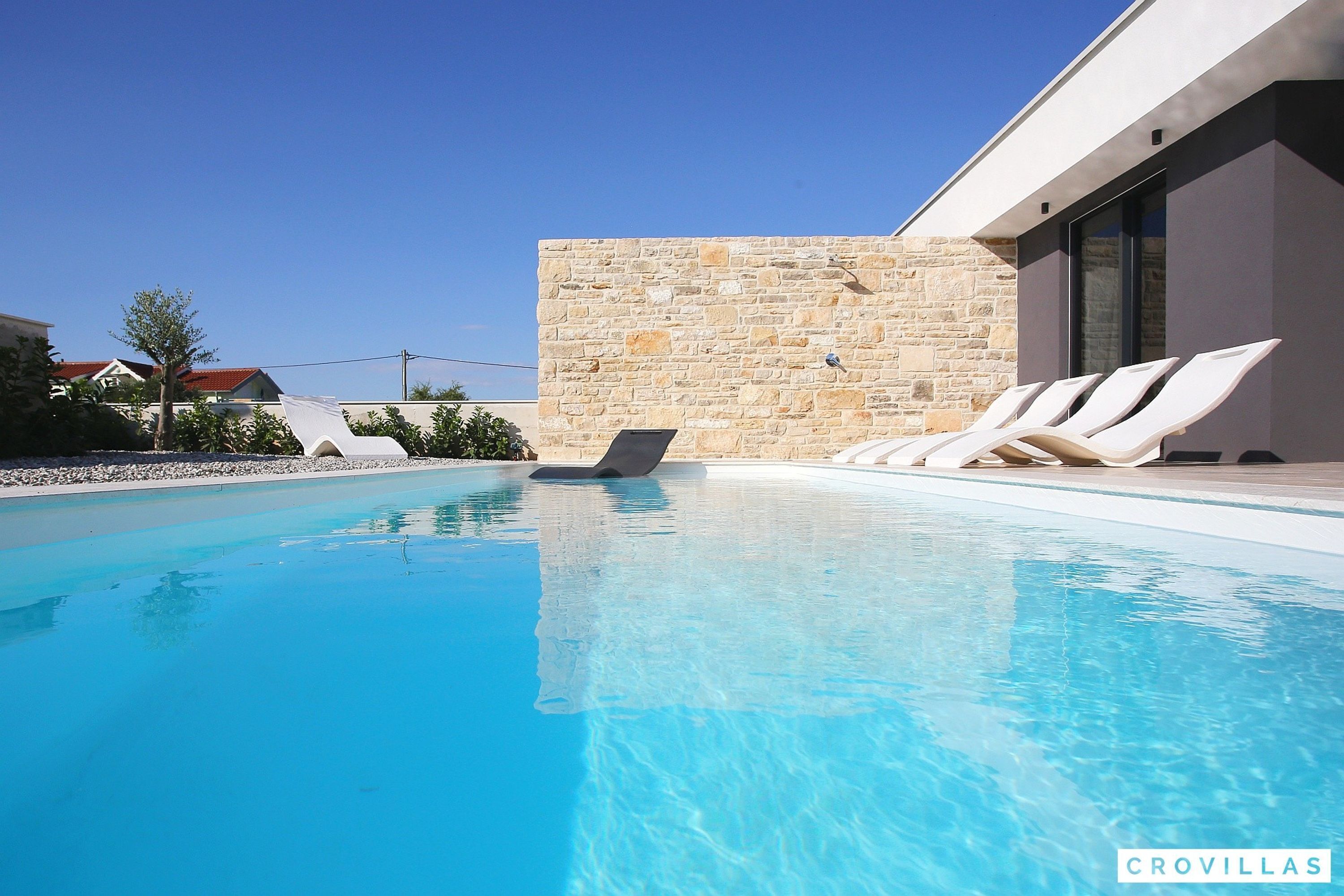 A swimming pool with lounge chairs and a stone wall.