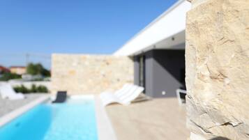 A modern poolside area with stone walls and lounge chairs.