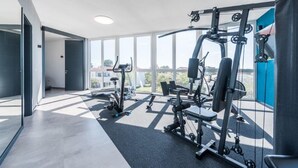 A modern gym with exercise equipment, large windows, and a view of buildings outside. - M8 in Vir With 2 Bedrooms and 2 Bathrooms (Vir)