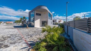 A modern building with a curved facade, a paved entrance area with palm plants, and a clear blue sky. - M8 in Vir With 2 Bedrooms and 2 Bathrooms (Vir)