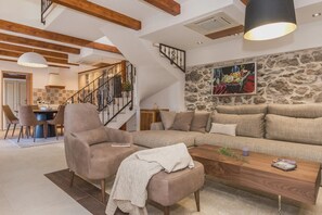 A spacious living area with a large sofa, a coffee table, and a chair. There is a staircase with a railing leading to an upper level.
