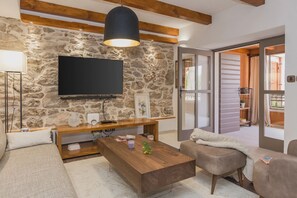A living room with a stone wall, a flat-screen TV, a wooden coffee table, and a sofa. - Ivanovi Dvori in Skradin (Skradin)