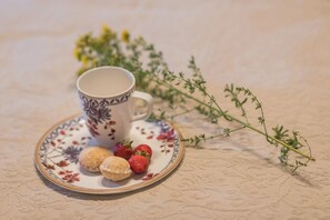 Uma chávena e pires com padrão floral, um prato com bolachas e morangos, e um ramo de tomilho numa superfície texturizada.