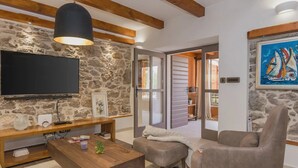 Un salon avec un mur en pierre, un téléviseur à écran plat, une table basse en bois, un canapé gris et un tableau représentant des voiliers.