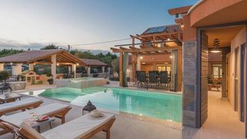 A poolside area with lounge chairs and a dining table, a covered patio, and a building entrance.