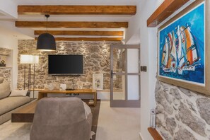 Een woonkamer met een stenen muur, een flatscreen televisie, een houten plafond, een bank, een bijzettafeltje en een schilderij van zeilboten.