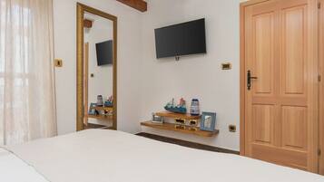 A bedroom with a bed, a TV mounted on the wall, a wooden door, and a shelf with decorative items.