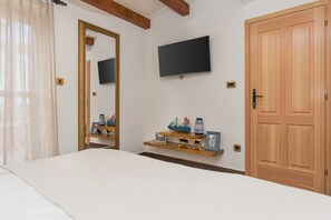 Quarto com cama, televisão fixada na parede, porta de madeira e prateleira com objetos decorativos.