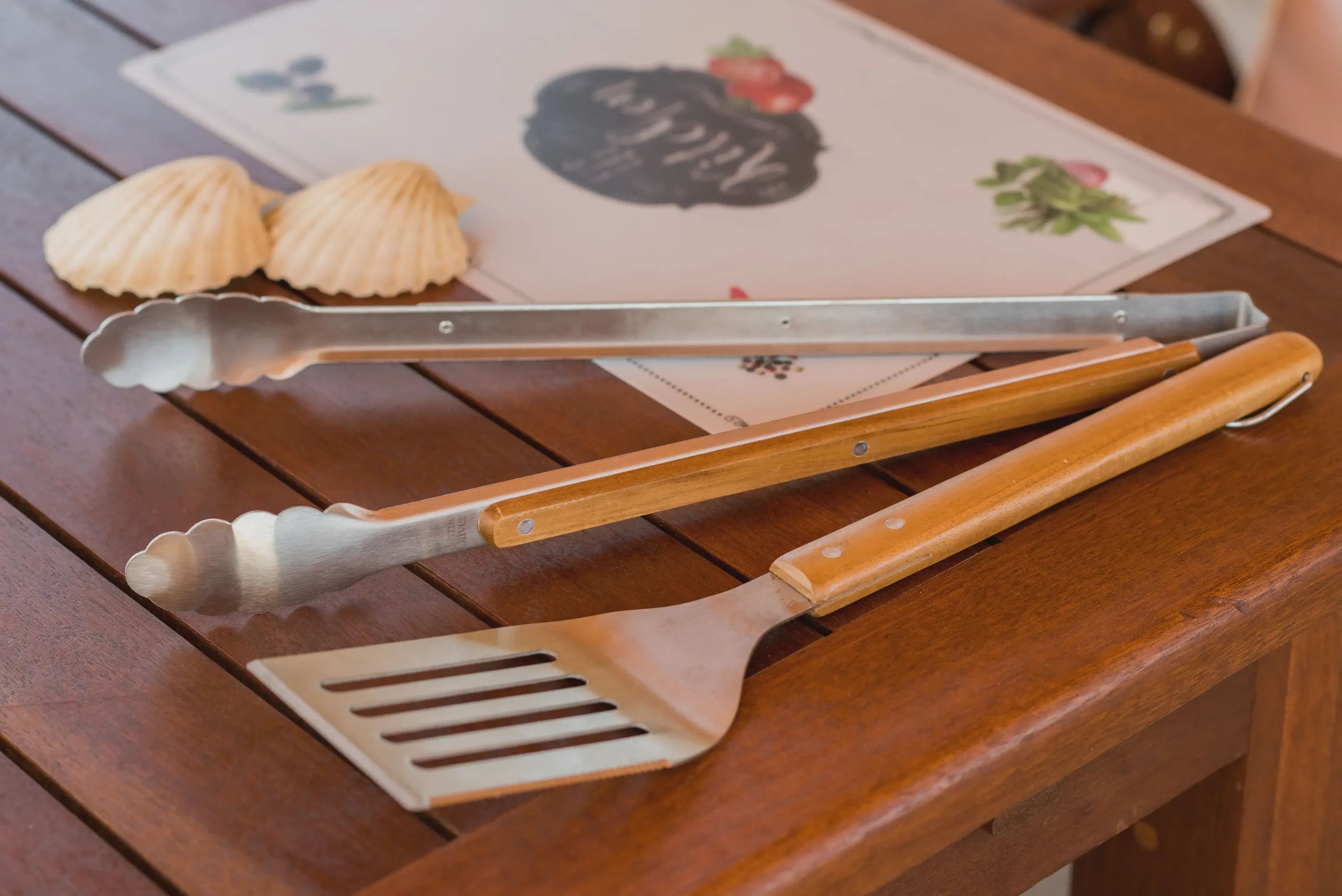 A wooden table with a metal spatula and tongs on it.
