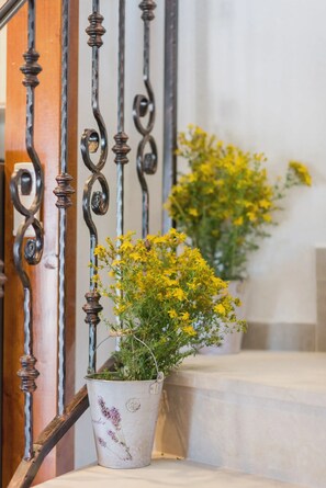 Un escalier avec des rampes en fer forgé et un pot de fleurs aux fleurs jaunes placé sur le palier.