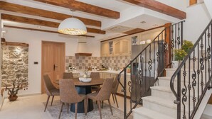 Une cuisine moderne avec des poutres en bois, un coin repas avec une table ronde et des chaises, et un escalier agrémenté de rampes décoratives.