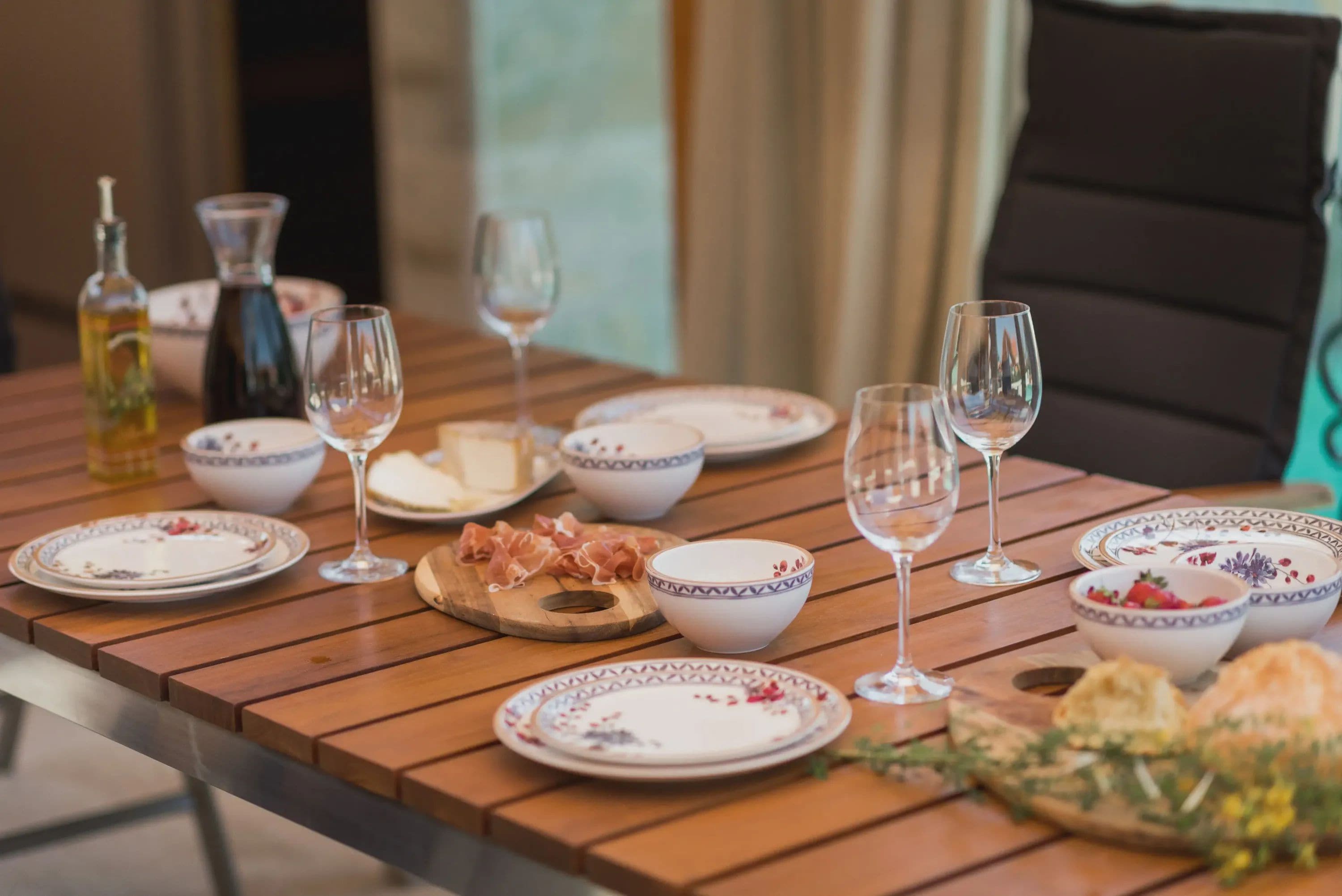 A wooden dining table set with plates, bowls, glasses, and a bottle of olive oil.