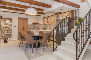 Een moderne keuken met houten balken, een eethoek met een ronde tafel en stoelen, en een trap met sierlijke leuningen.