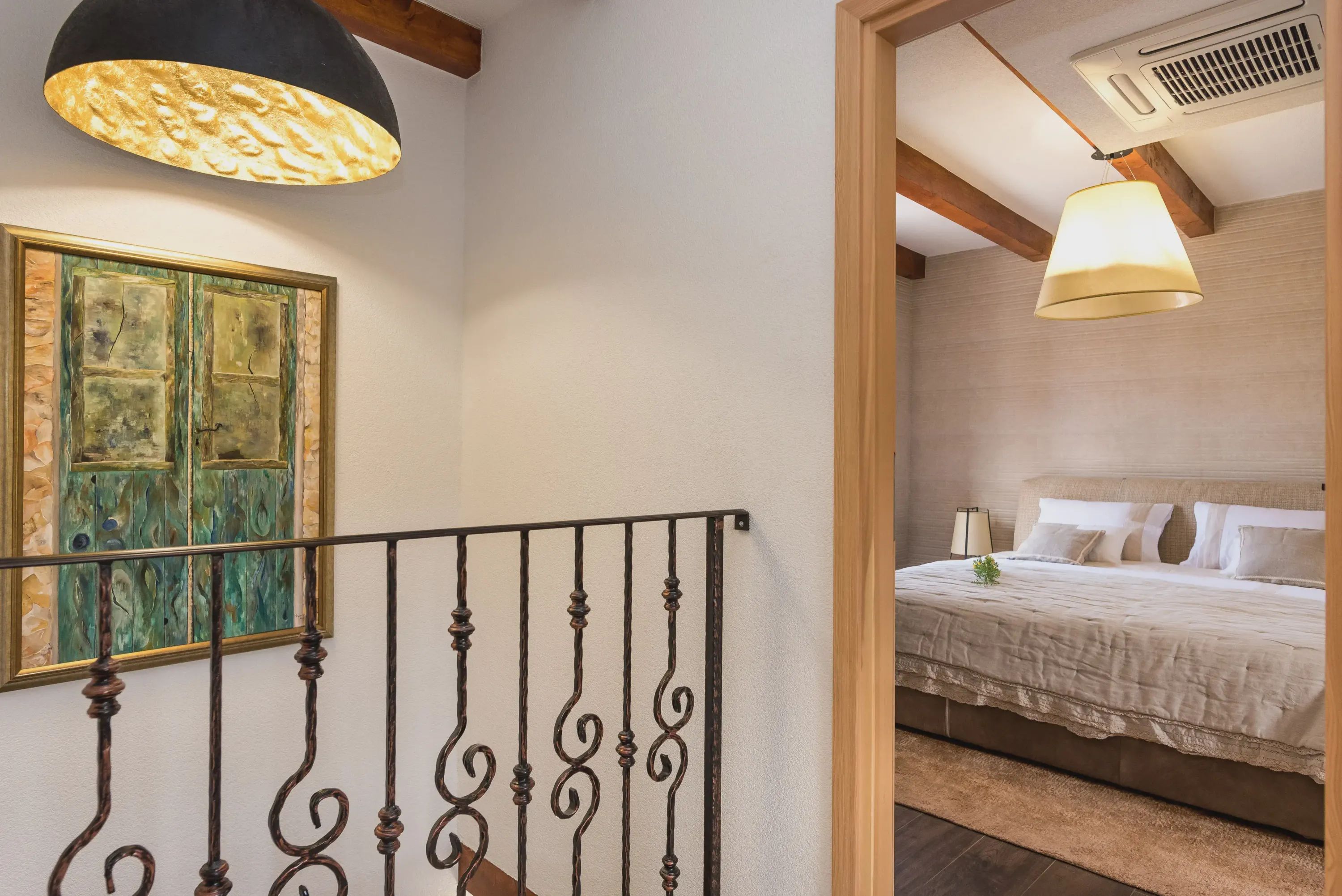 A bedroom with a bed, a bedside table, and a lamp. There is a painting on the wall and a window with curtains.
